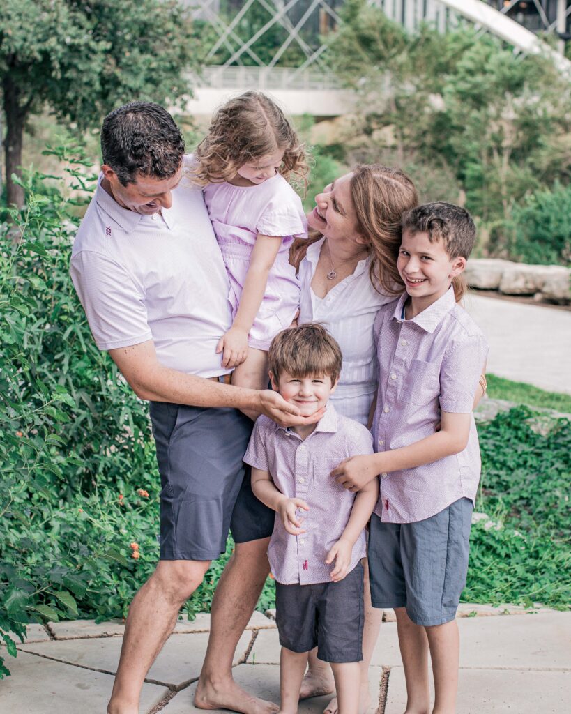 A happy family of five posing outdoors in casual clothes.