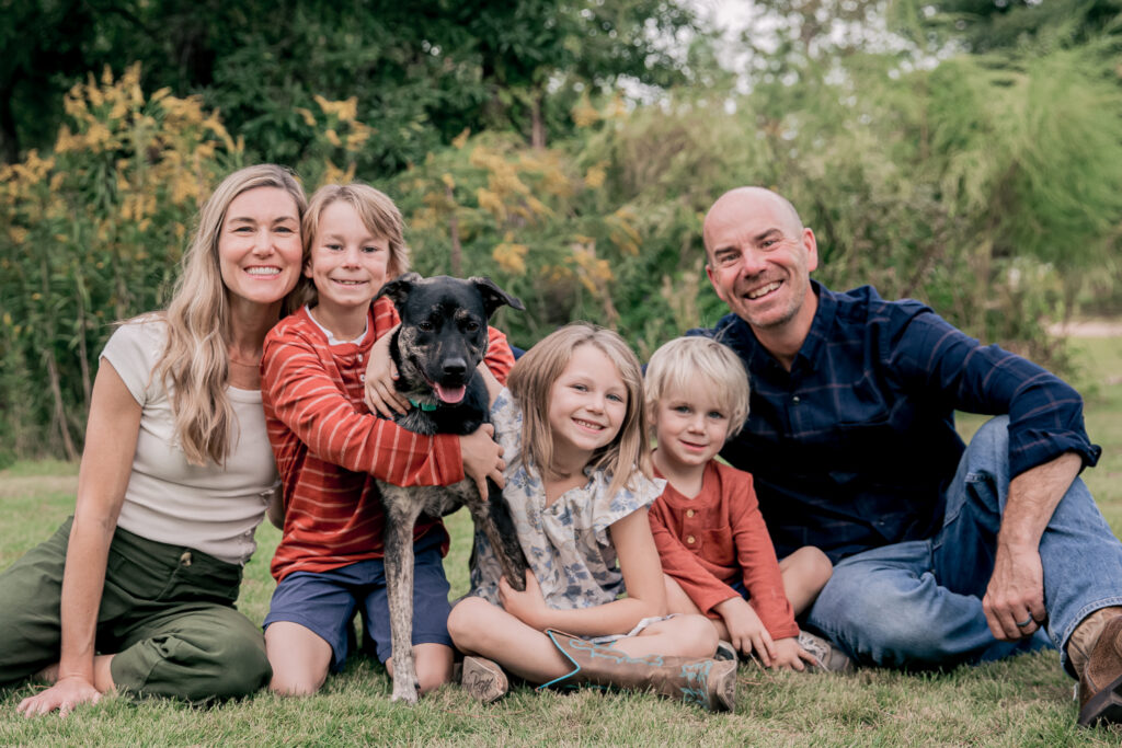 A happy family with two parents, three children, and their dog outdoors.