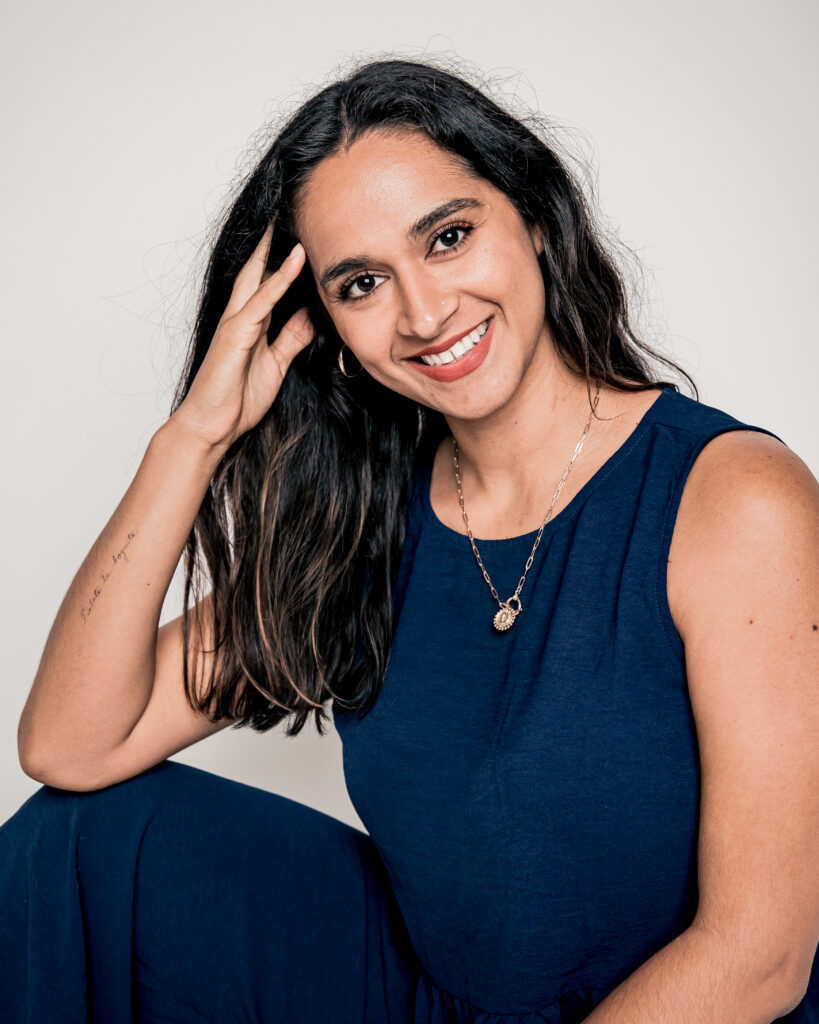 Smiling woman with long dark hair in a navy blue sleeveless dress.
