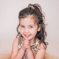 Smiling young girl with curly hair and a sparkly dress.