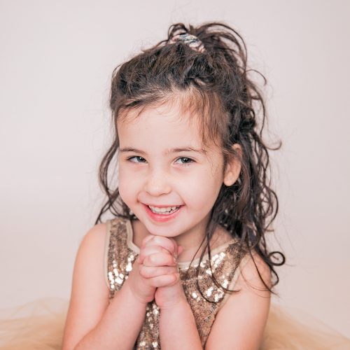 Smiling young girl with curly hair and a sparkly dress.