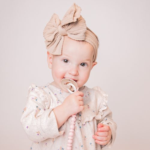Adorable baby girl with a big bow chewing on a pacifier.