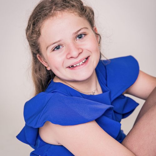 Smiling young girl in a blue dress looking at the camera.