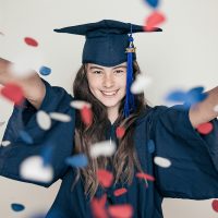 Happy graduate throws red and blue confetti in celebration.
