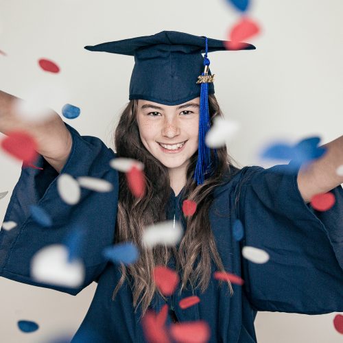 Happy graduate throws red and blue confetti in celebration.