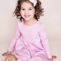 Smiling young girl in a pink dress with curly hair and a bow.