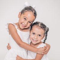 Two young girls in white dresses hugging and smiling joyfully.