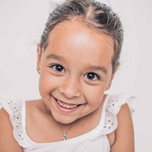 Smiling young girl in a white dress with braided hair.